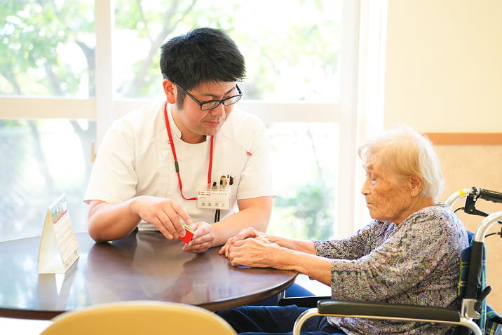 ヴィラとびしまの介護スタッフと車椅子の高齢者と向かい合い、認知機能トレーニングを行っています