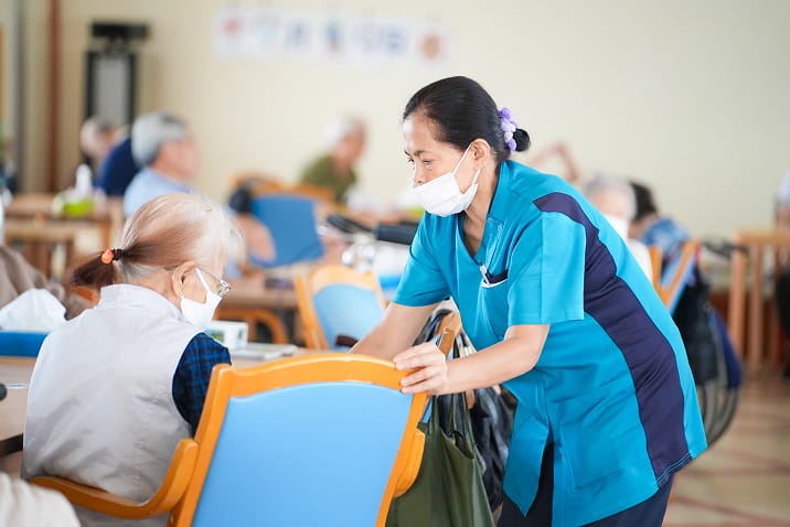 介護スタッフが座る利用者に寄り添い声をかけるコミュニケーションの場面