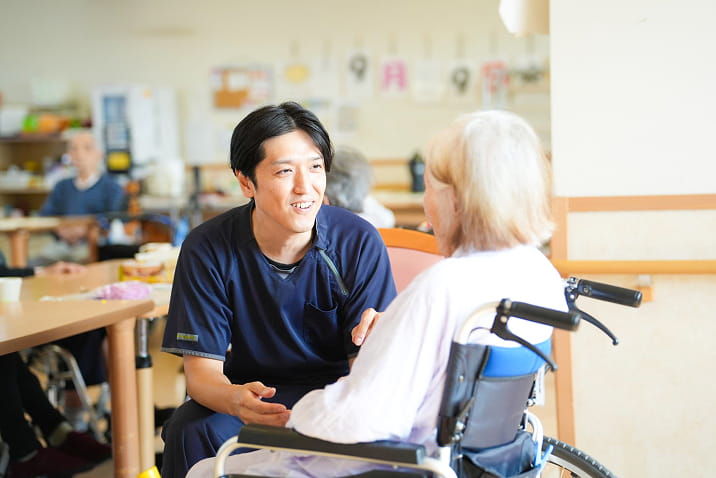 車椅子の利用者と向かい合い笑顔で会話する介護職員の様子