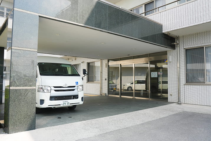愛知県飛島村の特別養護老人ホームやすらぎの里の外観。車寄せと送迎車が配置されたバリアフリー設計の入り口。高齢者や車椅子利用者が安心して利用できる施設外観