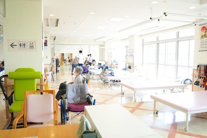 飛島村の介護施設内の活動室。高齢者がテーブルを囲んでパズルや手芸などのレクリエーション活動に取り組む様子。認知症予防や交流を目的としたグループ活動の場面